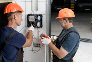Electricians are checking the voltage at the terminals of the electrical meter. They are using a multimeter.