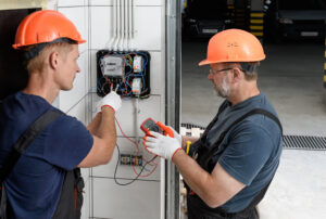 Electricians are checking the voltage at the terminals of an electrical meter. They are using a multimeter.