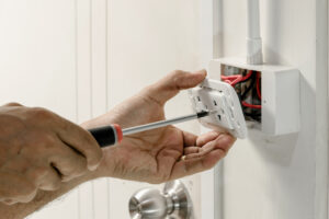 An electrician is using a screwdriver to attach a power cord to the wall outlet.